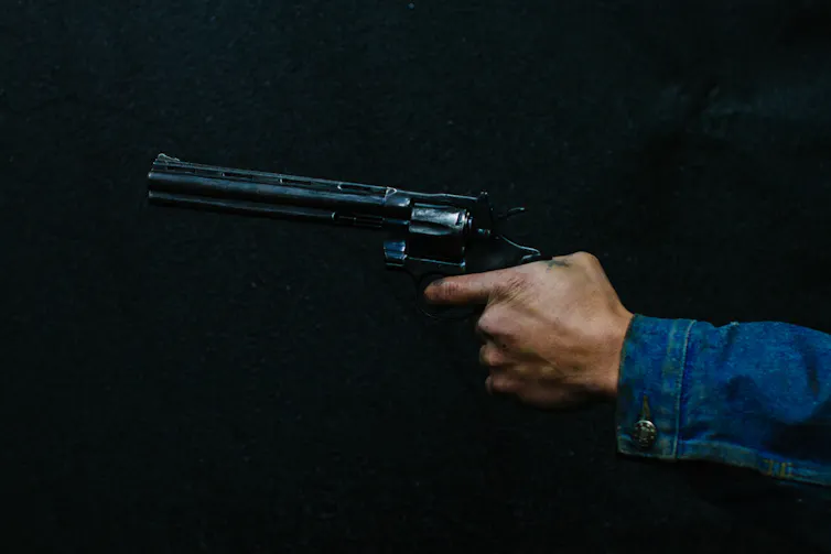 A hand holding a gun with the finger on the trigger.