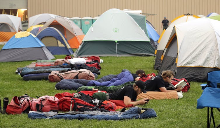 tents and sleeping bags set up on a lawn, firefighters rest on sleeping bags, photo