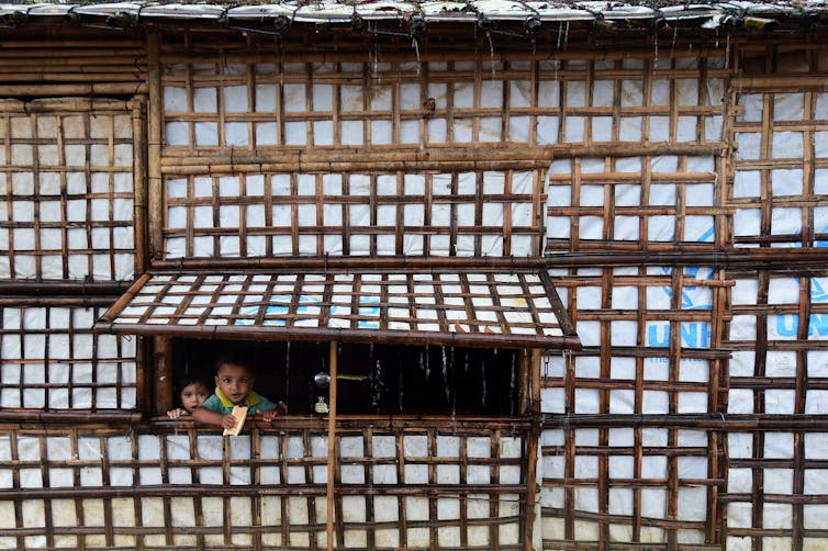 Two toddlers looking out window of house, one eating a snack, photo