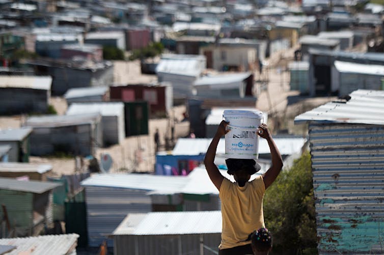 A woman carries a bucket of fresh water to an informal settlement in Khayelitsha, near Cape Town. South Africa has the widest wealth gap in the world. Photo by RODGER BOSCH/AFP via Getty Images