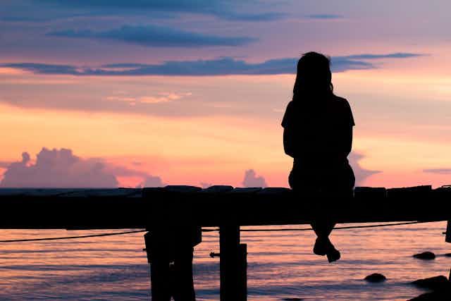 Image of a woman sitting alone on a bench in sunset.
