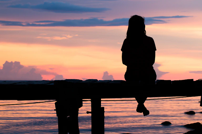 Image of a woman sitting alone on a bench in sunset.