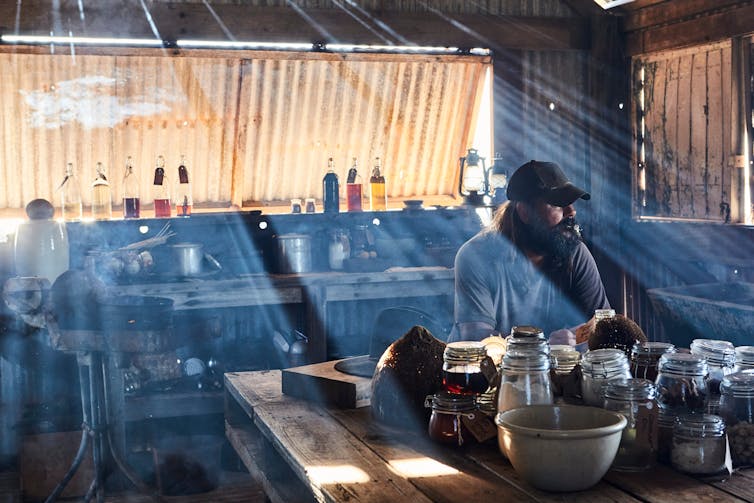 A Man Sits In Moody Shadows In A Tin Shack.