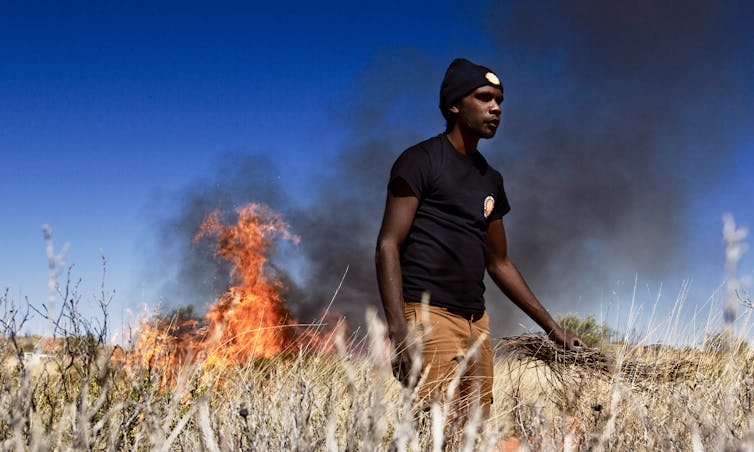Indigenous man in front of small grassland fire 