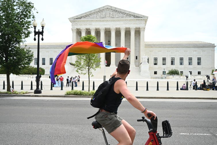 A man waves a rainbow flag as he rides by the Supreme Court on June 15, 2020. JIM WATSON/AFP via Getty Images