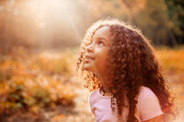 A young girl looking up to the sun.