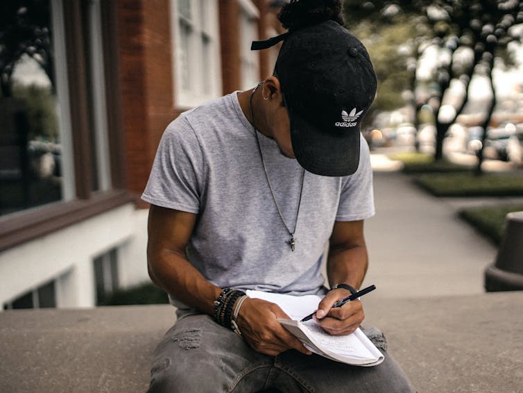 A young Black man writes in a notebook.