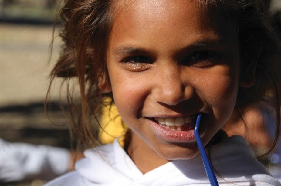 Girl smiling and showing teeth with toothbrush in her mouth.