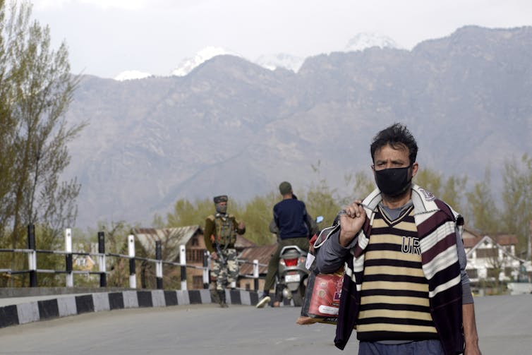 Kashmiri man wearing face mask with soldiers in the background