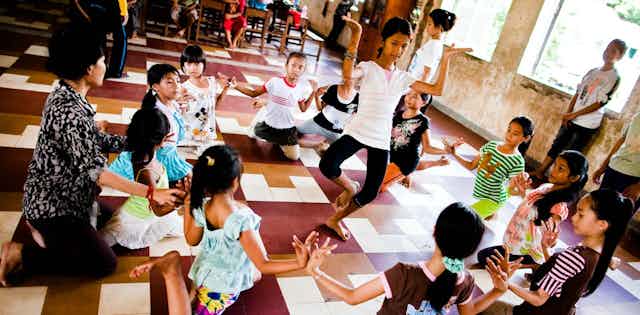 Children sitting in a circle watch a dancer in the centre.