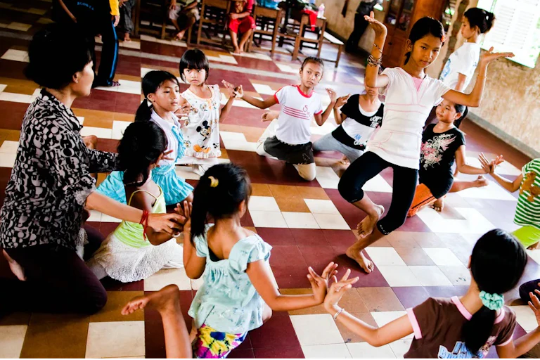 Children sitting in a circle watch a dancer in the centre.