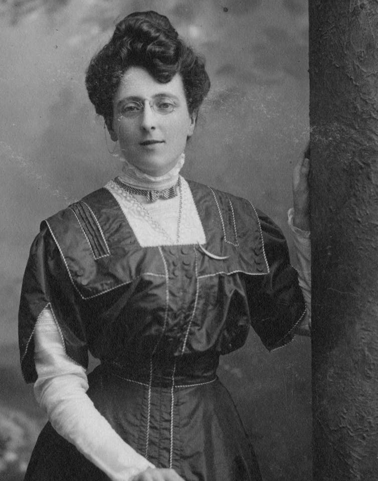 A black-and-white photo of L.M. Montgomery. She has her left arm propped against a wall.
