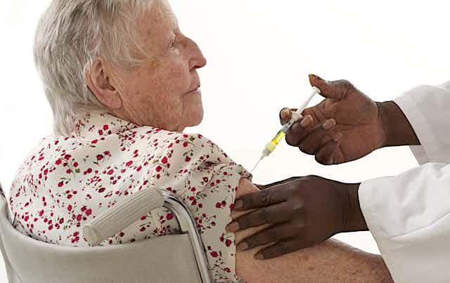 An older woman receives an injection in her upper arm from a health-care worker