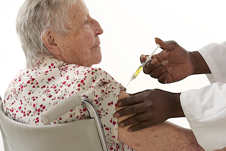 An older woman receives an injection in her upper arm from a health-care worker
