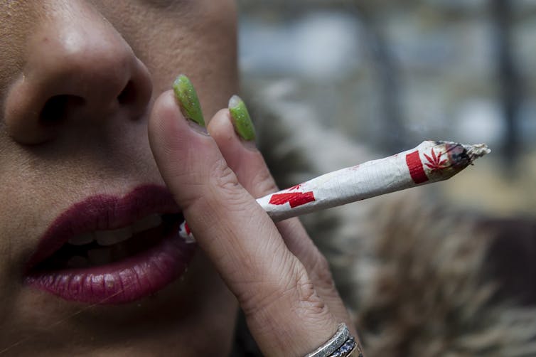 A woman with green nail polish smokes a joint rolled with a paper that has Canadian flags on it.