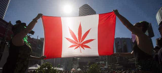 People at a gathering hoist a Canadian flag with a marijuana leaf instead of a maple leaf in the centre.
