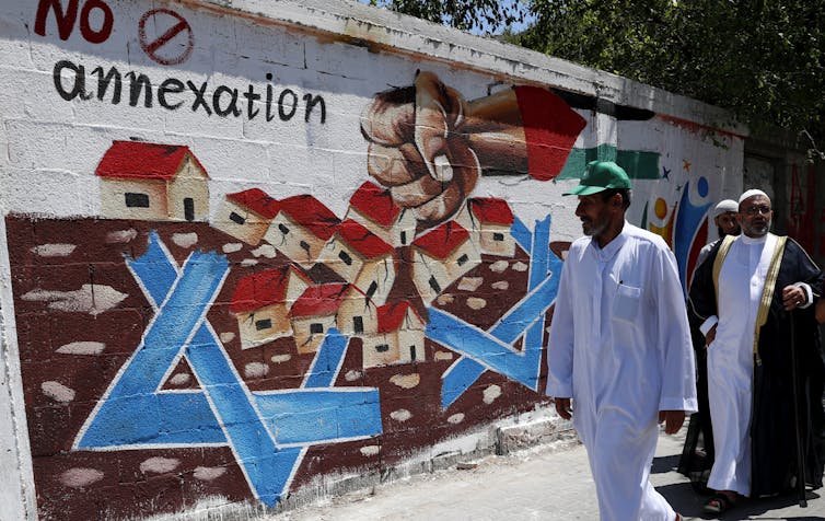 Hamas supporters walk past a sign opposing Israel's annexation plans