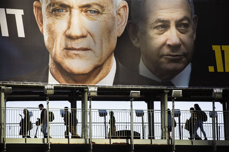 People walk past an election sign showing Netanyahu and Gantz