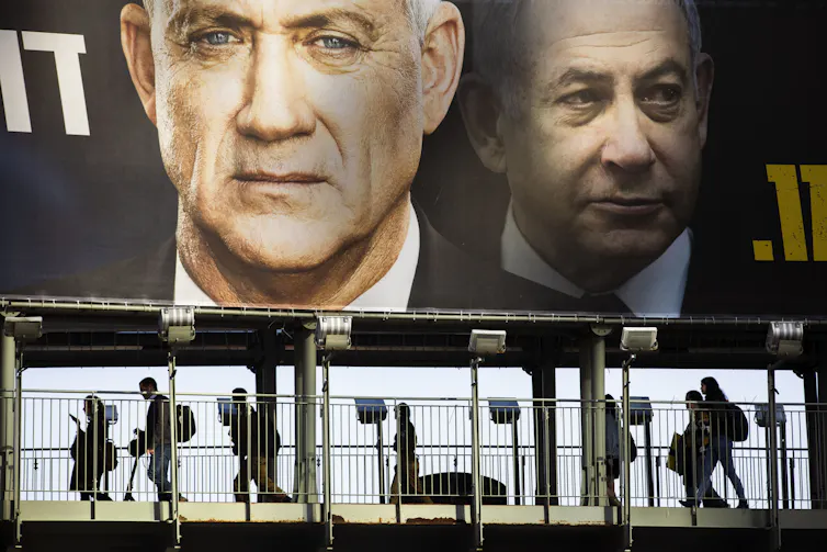 People walk past an election sign showing Netanyahu and Gantz
