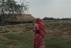 A woman dressed in a pink sari walks across a field.
