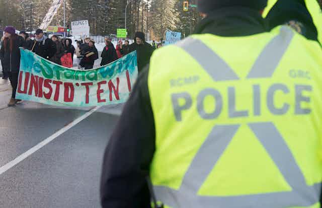 Protesters walk along a road carrying signs as a police officer looks on
