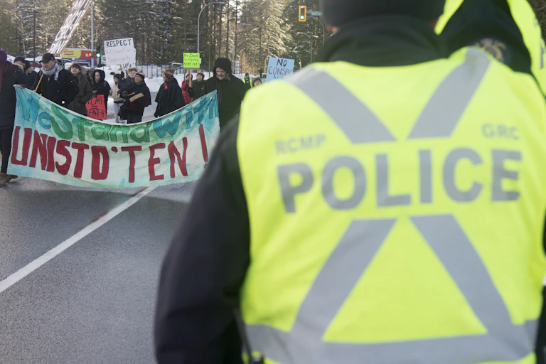 Protesters walk along a road carrying signs as a police officer looks on