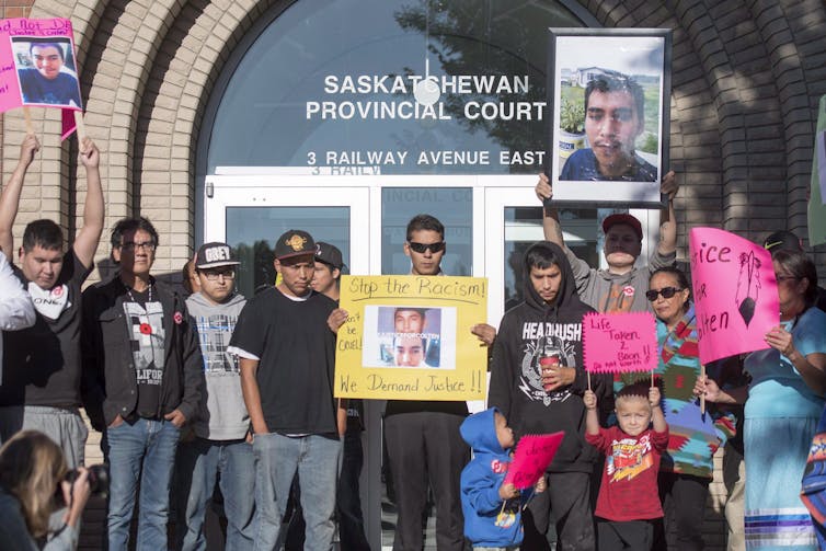 A group of people carrying signs and pictures of Colten Boushie in front of the courthouse.