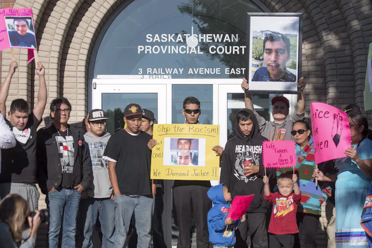 A group of people carrying signs and pictures of Colten Boushie in front of the courthouse.
