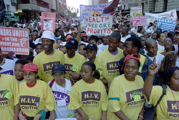 Protesters wearing yellow 'HIV Positive' shirts hold signs and banners