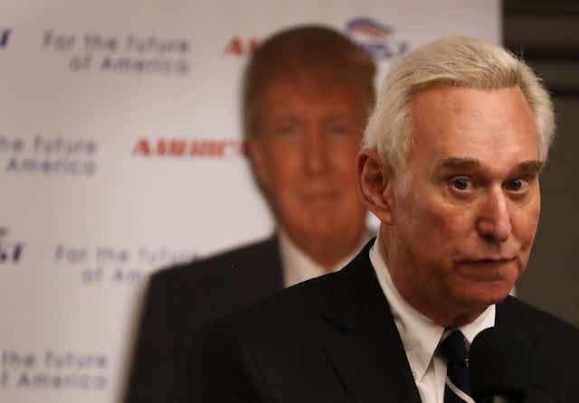 Roger Stone in front of a poster showing an image of Donald Trump.
