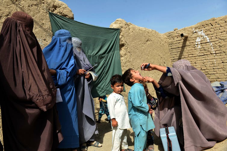 Afghan women in burqas vaccinate young boys