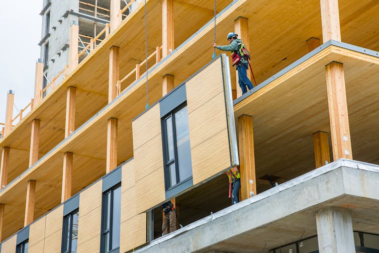 A construction worker guides a prefabricated building panel into place.