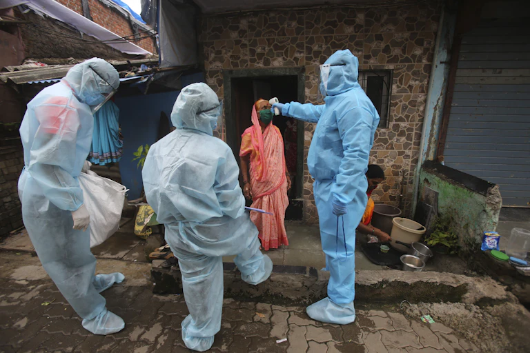 Three people in full protective equipment aim a temperature gun at a woman wearing red
