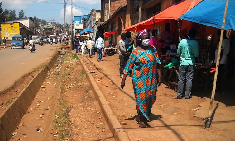 Femme se promenant masquée dans les rues de Bukavu, avec des passants en arrière-plan.