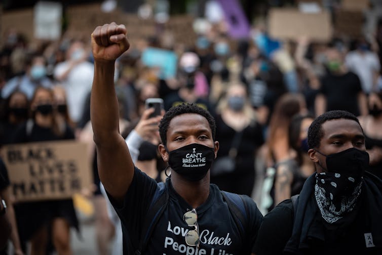 A young Black man raises his arm during a Black Lives Matter protest