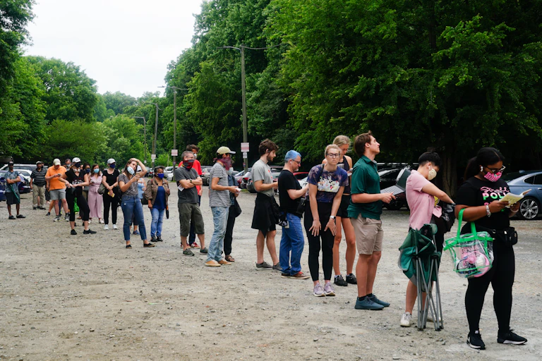 A line of people waiting in a muddy parking lot.