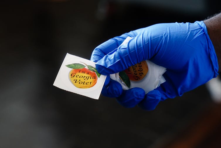 A gloved hand holding out a sticker reading 'I'm a Georgia voter.'