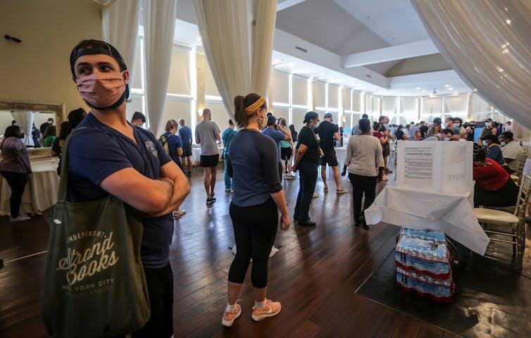 A man stands at the end of a line in a crowded room.