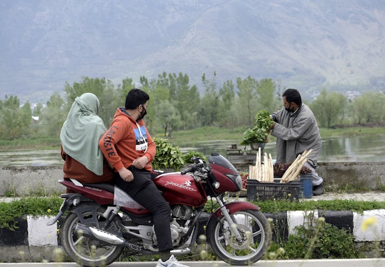 Man and woman on motorcycle near a worker and a lake
