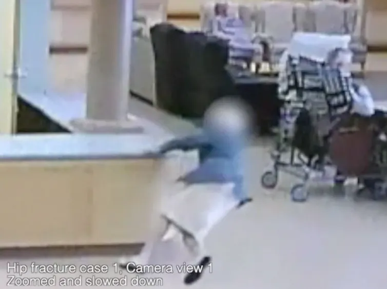 A woman in a large room reaches for a counter to try to steady herself as she falls to the floor