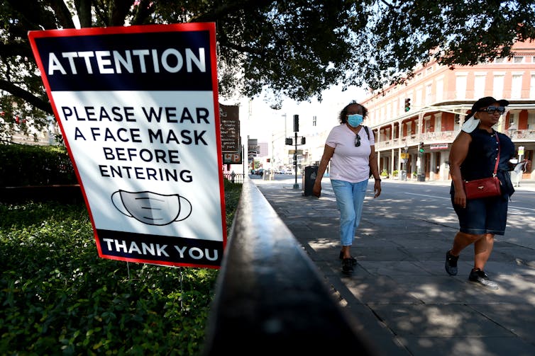 streetscape with people walking and sign asking for masks before entering