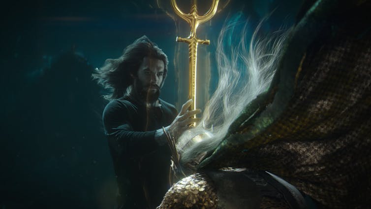 Aquaman holds a gold staff.