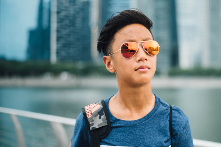 A teen boy in sunglasses with a knapsack stands outside.
