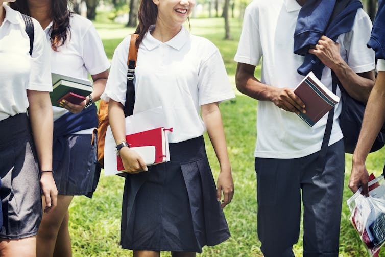 A group of teens with school books and bags walk outside