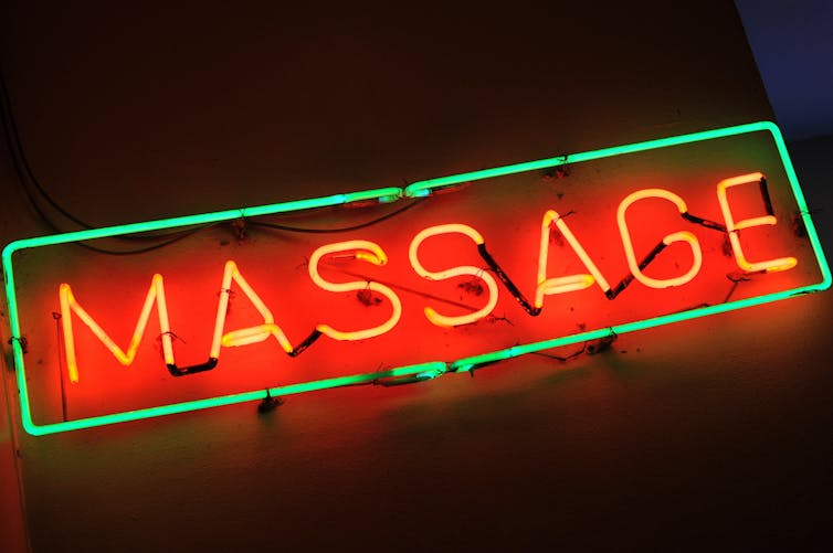 A neon sign says 'massage' in red capital letters with a green border.
