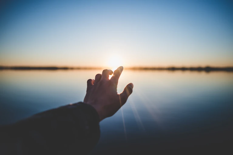 A hand reaching for the sun on the horizon.