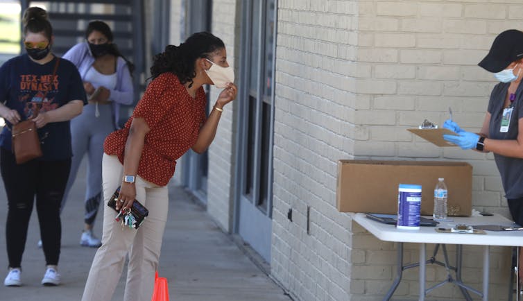 A woman asks a health care worker a question while staying socially distanced.