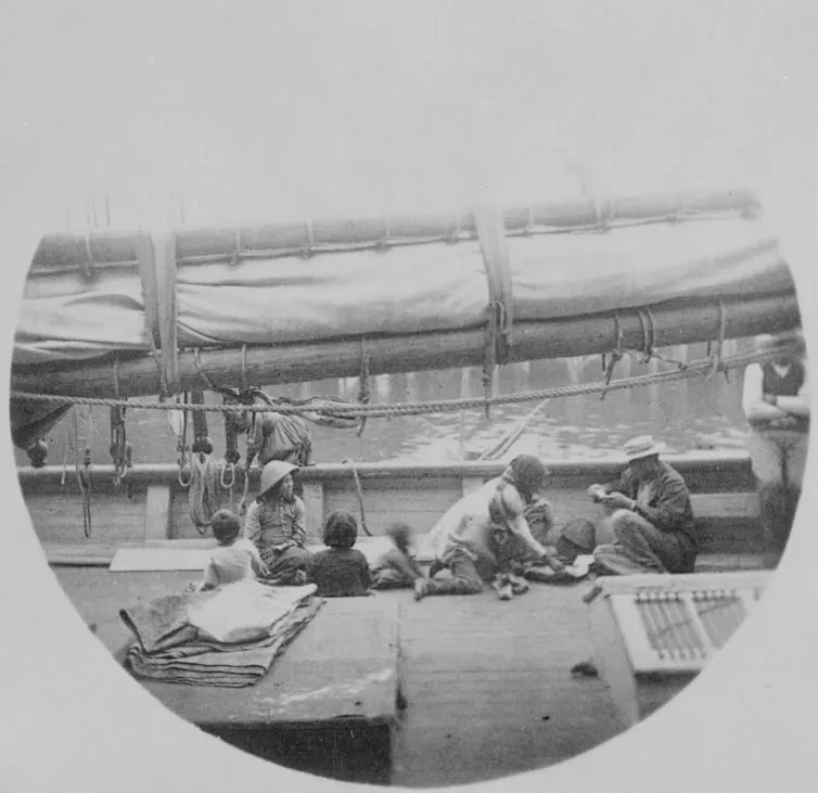 A black and white photo showing a group of Chinese people sitting on the deck of a ship.