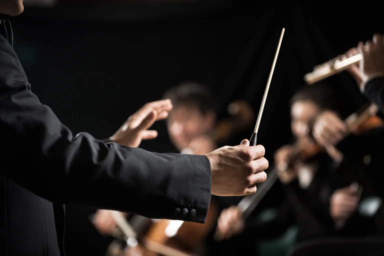 A music conductor guides an orchestra with a baton