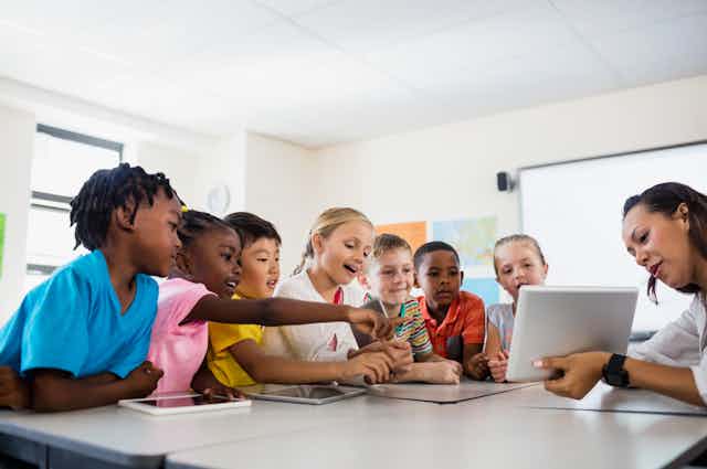 children looking at digital tablet held by teacher